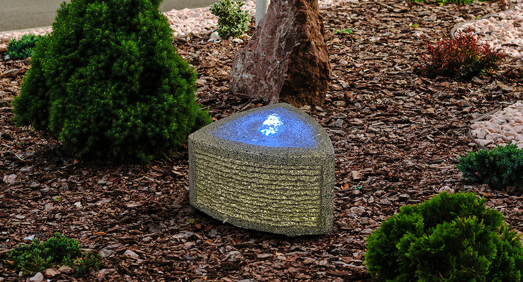 Triangular carved granite fountain with LED light in outdoor garden.