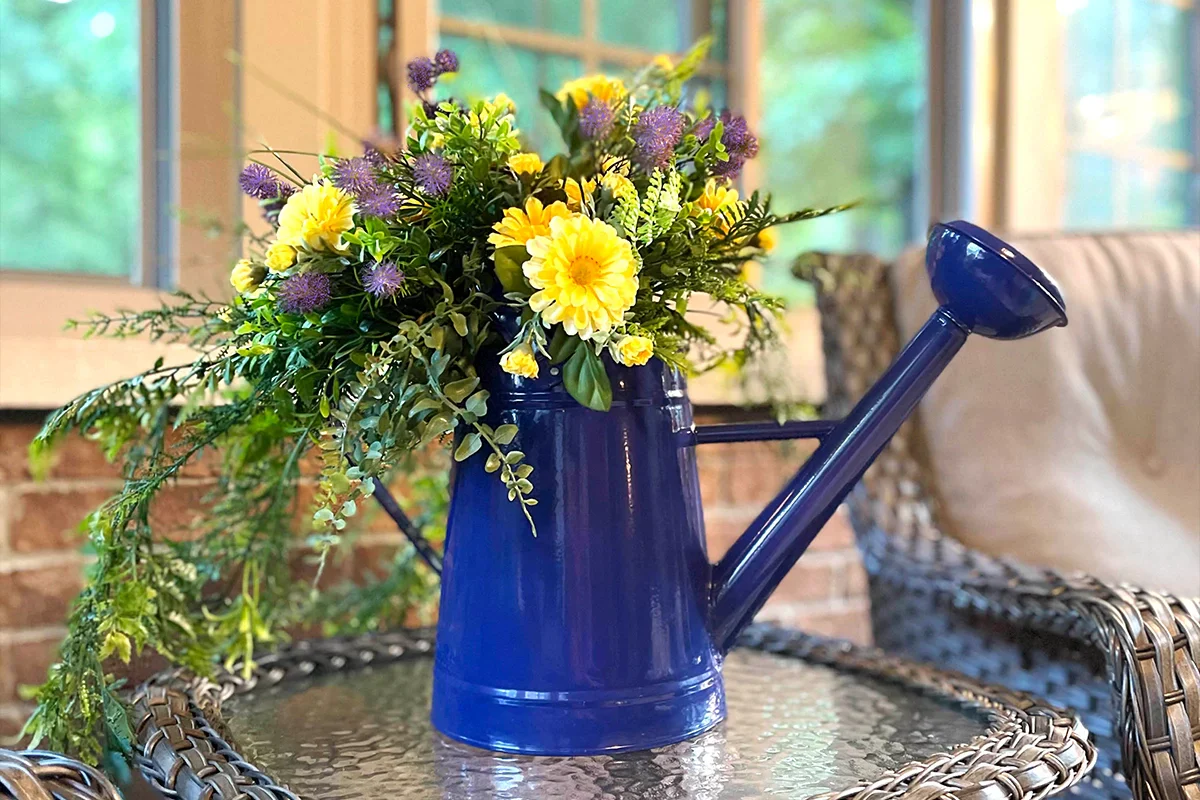 Fresh cut yellow flowers in a beautiful blue metal watering can sitting on a patio table.