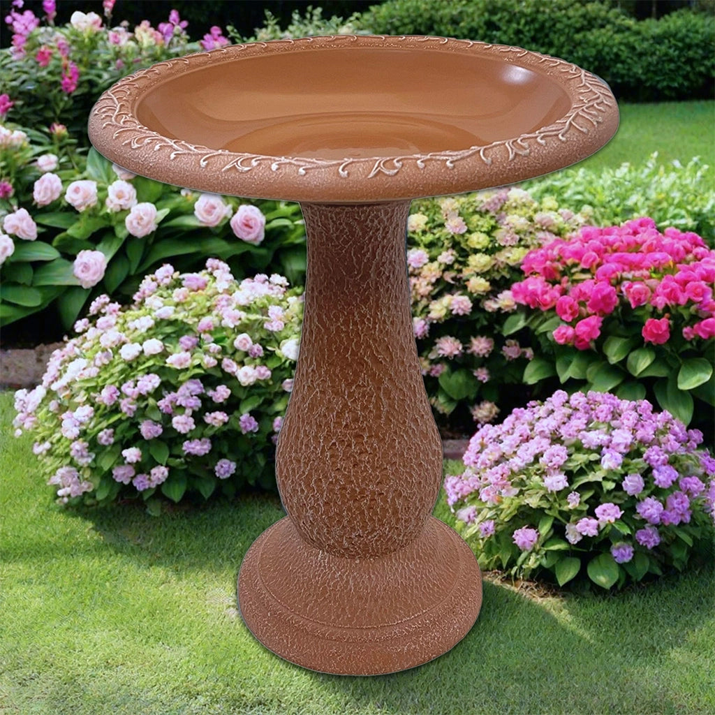 Terracotta colored fiber clay birdbath in a beautiful landscape of pink and purple flowers.