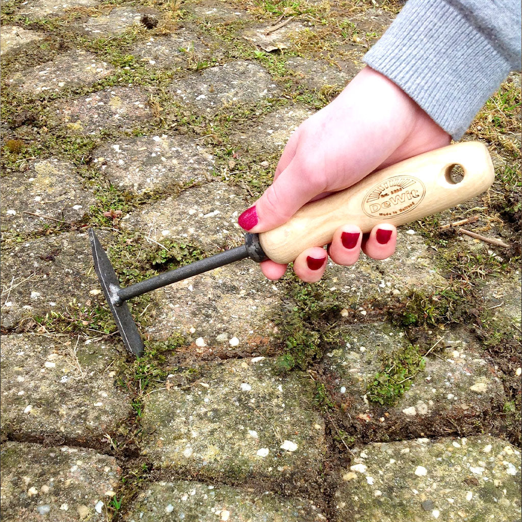 A DeWit patio knife removing weeds from the crevices of a cobblestone patio.