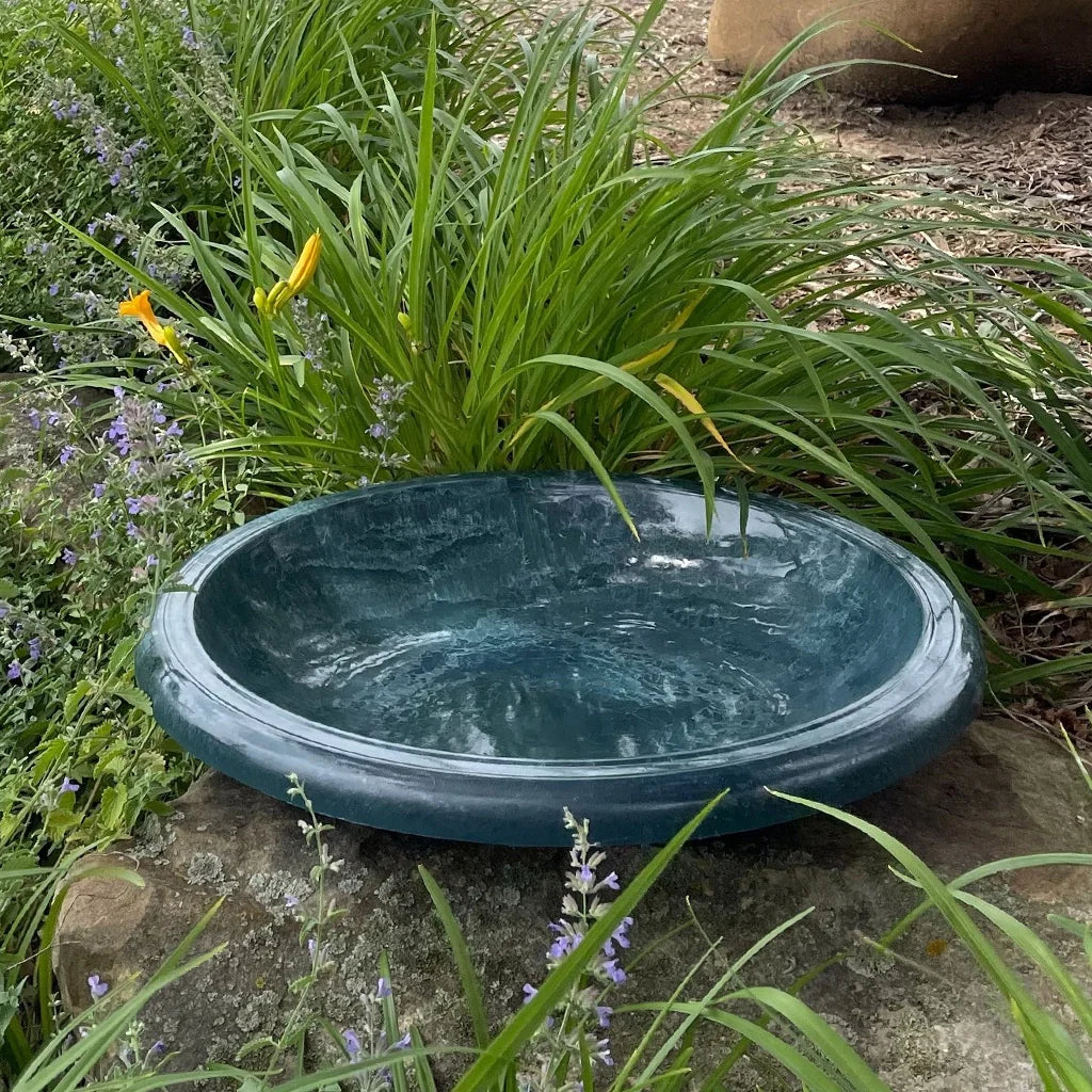 Birdbath bowl perched on a boulder in beautifully landscaped flower bed.