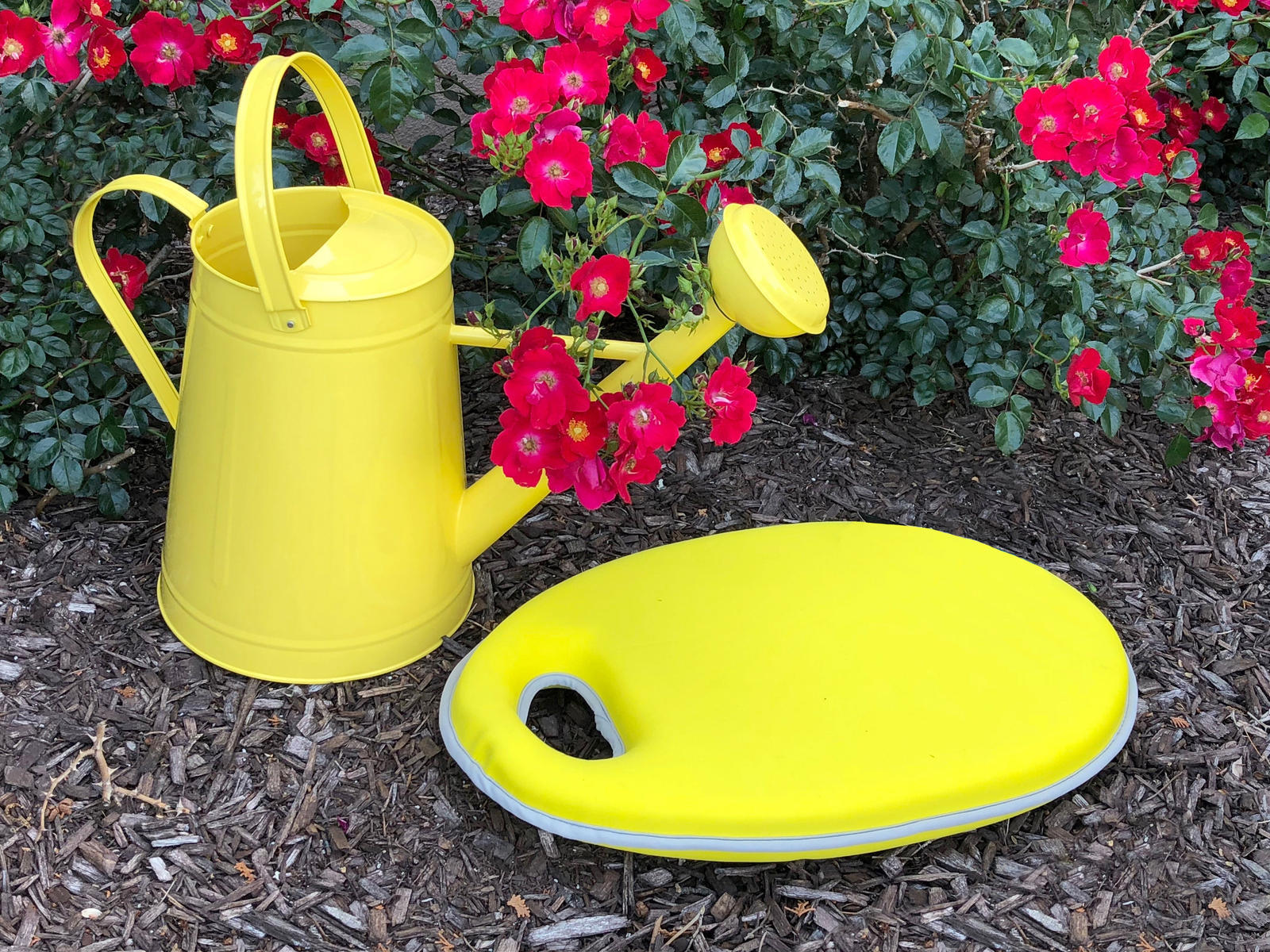 Yellow metal watering can and memory foam kneeling cushion set in garden.